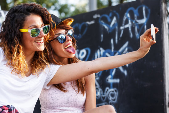 Two female skaters friends sitting on ramp and hangout at the skate park .Taking selfie.