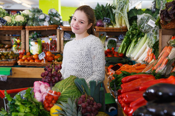 Happy girl among fruits and vegetables on store shelves