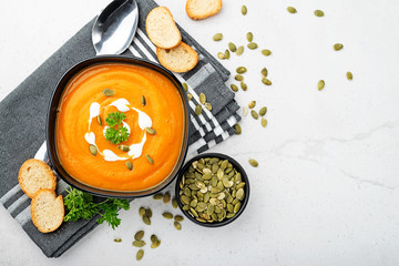 Pumpkin and carrot soup with cream and parsley on gray background. Top view