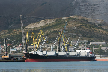 Loading cranes at the seaport unload or load a cargo ship. Cargo ship for bulk cargo in a seaport against the background of mountains