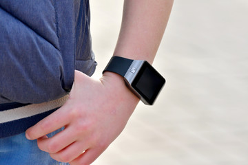 A smart watch on the boy's hand in a blue jacket with rolled up sleeves