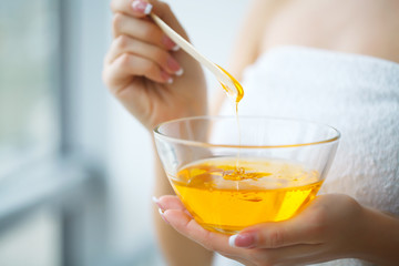 Women hold orange paraffin wax bowl. Woman in beauty salon