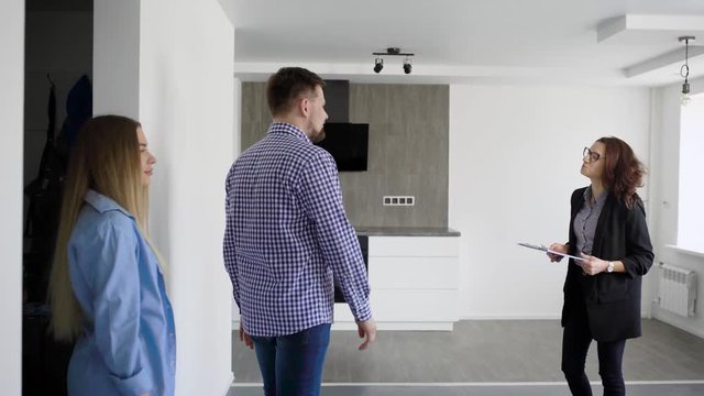 a young married couple looks at the kitchen in a newly built and refurbished house, the realtor demonstrates housing for purchase