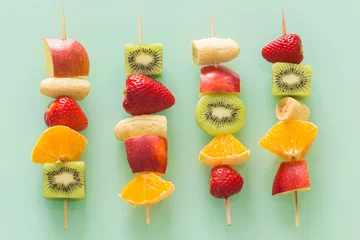 Rolgordijnen fruit skewers the concept of healthy eating / pastel green glass background. © Rochu_2008