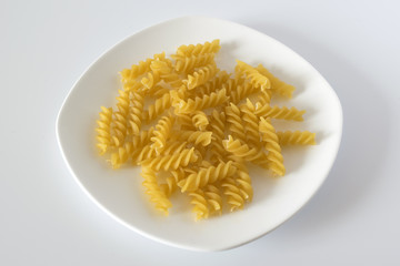 Uncooked spiral pasta on a white plate. Macro