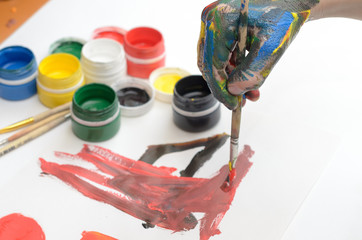 A child's hand in paint paints gouache on white paper.