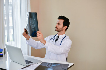 Smiling doctor posing in the office, he is wearing a stethoscope, medical staff on the hospital background