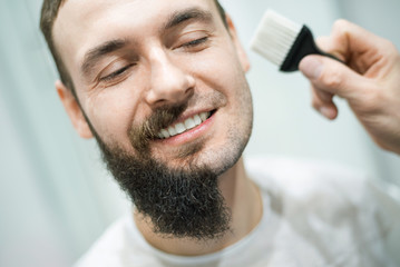 Handsome bearded man is getting shaved by hairdresser at the barbershop