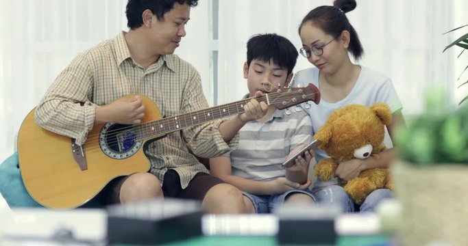 Happy asian Father playing guitar for his family at home