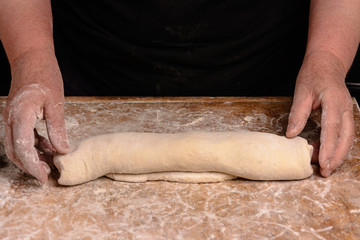 An elderly woman rolls out of a raw batter for baking on a dark background