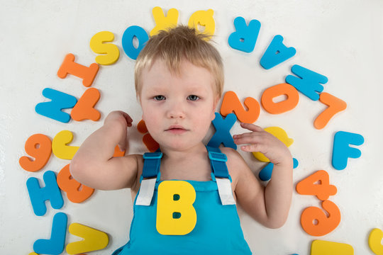 Happy charming Caucasian blond's kid in colored clothes playing with plastic letters. Learning the alphabet, preparing for school. Education for kindergarten and preschool children. White background