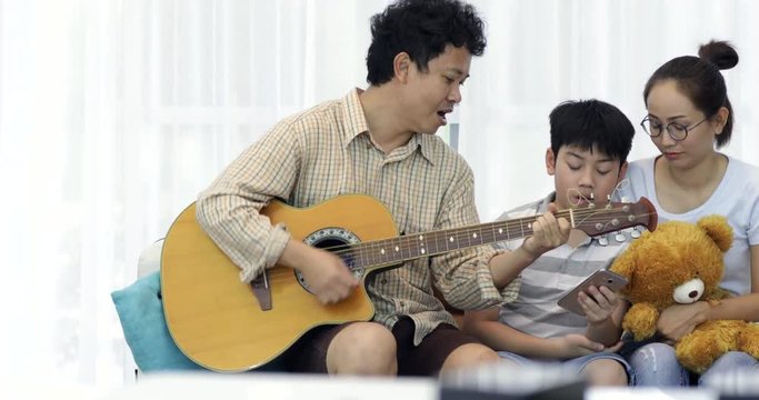 Happy asian Father playing guitar for his family at home