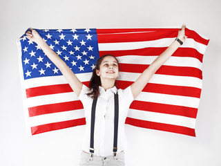 I love America. Happy young smiling woman in jeans and white Tshirt holding up American flag and looking up while standing against a light gray background.