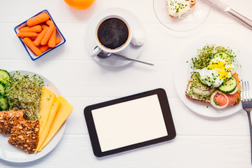 Top view tablet with blank copy space screen and healthy breakfast with coffee on the white wooden table. Work, day planning, edication process during eating. Selective focus.