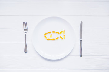 Top view Cod Liver Oil Capsules, Omega 3, Vitamin D in the fish shape on white round plate served...