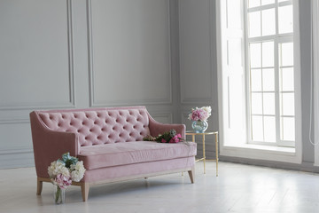A large beautiful pink sofa stands in a spacious living room in a classic style.