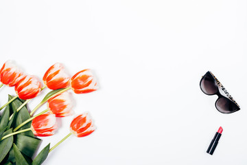 Top view frame of red tulips, woman's sunglasses and opened lipstick