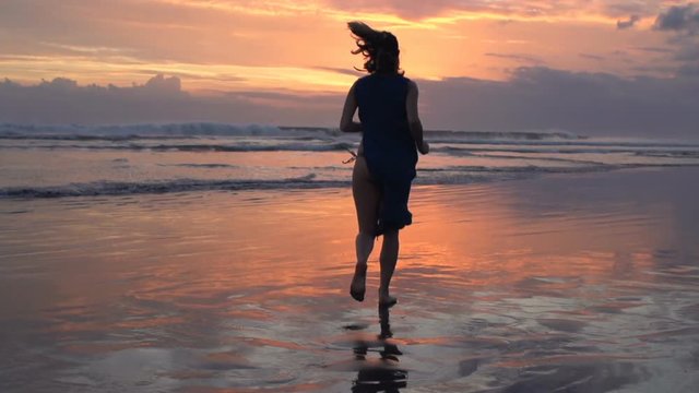 Silhouette of woman running on beach during sunset
