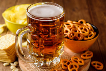 Mug of beer and snacks on wooden background