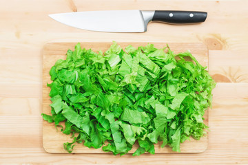 Close-up on a wooden table is a wooden cutting board on which lies chopped lettuce leaves and next to a large cutting knife. The concept of self-cooking vegetarian food at home. Healthy lifestyle