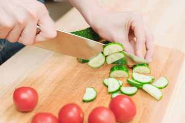 close-up of female hands cut into fresh cut cucumbers on a wooden cutting board next to pink tomatoes. The concept of homemade vegetarian cuisine and healthy eating and lifestyle