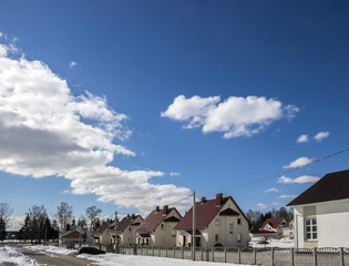 sunny day street snow lies with cottages car costs road blue sky clouds background horizontal 