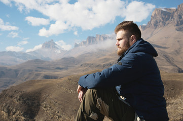 A portrait of a stylish bearded hipster sitting on a rock against the backdrop of epic rocks and...