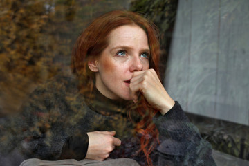 Hübsche rothaarige Frau schaut nachdenklich aus einem Fenster