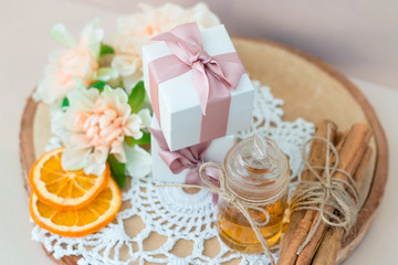 Fototapeta na wymiar Made at home from orange oil with cinnamon perfume in a glass jar. Slices of dried orange, dried cinnamon and flowers. Gift box with jewelry charm bracelet is on the table. Present for every woman.