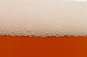 Bubbles from a beer froth close-up on half a glass.