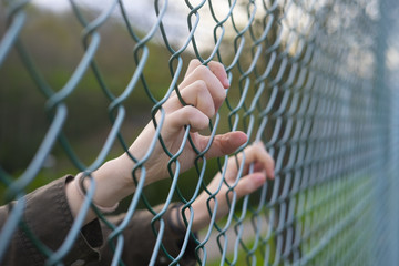 Hands of a refugee woman on a wire fence, a girl imprisoned and deprived of freedom