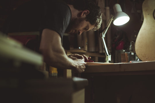 Side View Of Man Shaving Guitar Wood At Workshop