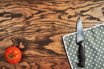 Top view of tomato, black knife with napkin on the wooden background