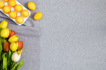 Yellow Easter eggs with a bouquet of tulips on the table top made of artificial acrylic stone. The creative concept of the celebration of Easter, an unusual approach to decorating