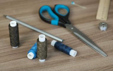Fototapeta na wymiar Sewing supplies scissors, thread, bobbins, pencil, a ruler on wooden table.