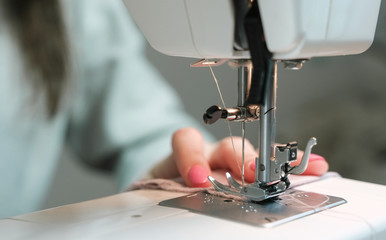 Woman sewing light fabric on a sewing machine close-up.