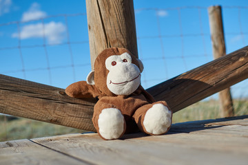 Closeup of a lovely brown and white toy monkey smiling happily sitting on a wooden floor and leaning comfortably on a wooden railing