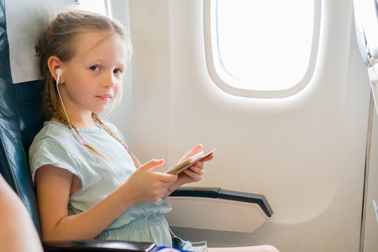 Adorable little girl traveling by an airplane. Cute kid with laptop near window in aircraft