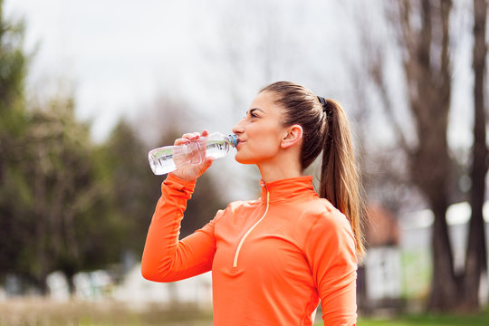 Active young woman taking break after running and drinking water