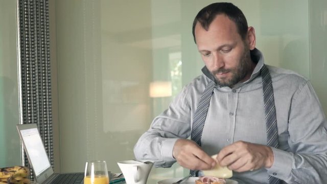 Young businessman preparing and eating breakfast by table at home
