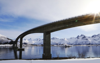 Bridge in the Lofoten islands in winter with lens flare.and mountains reflection.