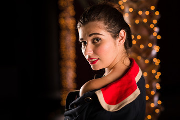 Young caucasian woman dressed in 1960 style poses in a room filled with fairy lights