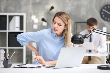 Young woman suffering from back pain in office