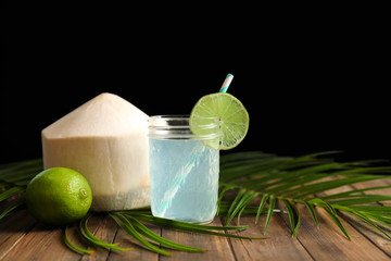 Jar with fresh coconut water and lime on table against black background