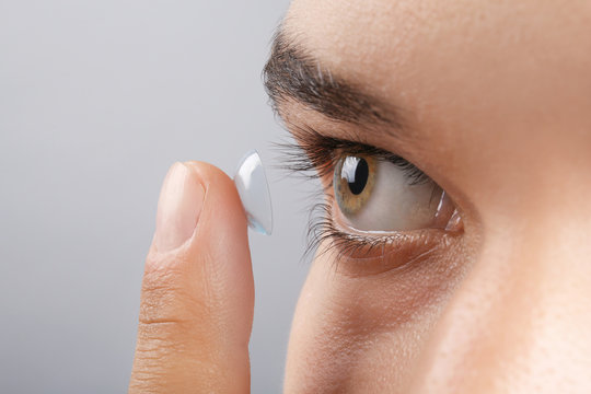 Young Man Putting Contact Lens In His Eye On Grey Background, Closeup