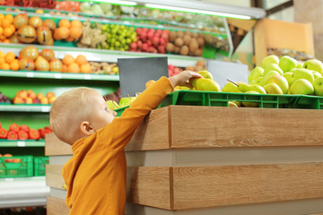 Cute little boy choosing pears in supermarket