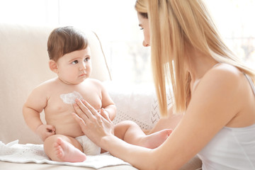 Obraz na płótnie Canvas Woman applying body cream on her baby indoors