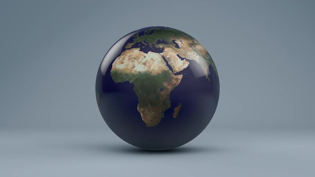 A glass orb Planet Earth rotates on a pastel blue cyc (Loop).