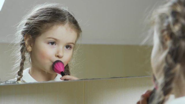 Adorable little girl doing makeup in front of mirror