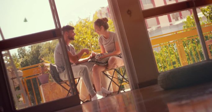 Relaxed young hipster couple having fun together sitting on balcony